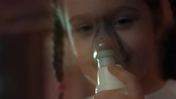 Little Girl Makes Inhalation Using a Compressor Inhaler While Sitting on a Sofa