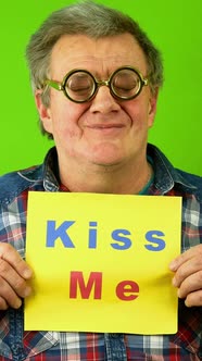 Caucasian Mature Adult Man Smiling and Point Finger at Plaque Lettering Kiss Me