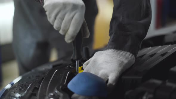 Close-up of Male Hands in Protective Gloves Using Screwdriver To Tighten Screws in Open Car Hood