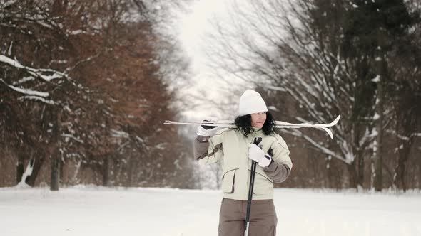 Sporty Mature Woman with Skis Standing in Forest in Winter