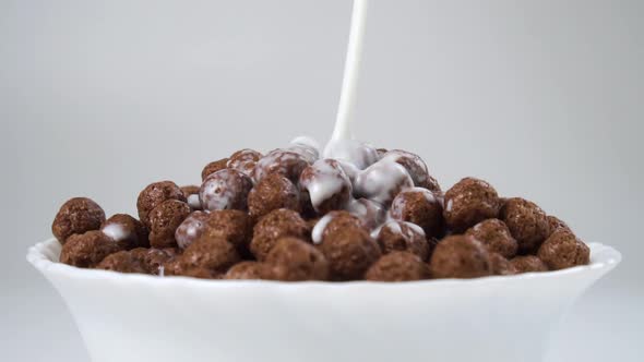 Fresh milk is poured into a bowl full of chocolate cereal balls