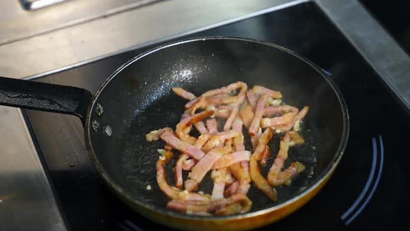 Frying bacon pieces in a pan. Crispy pieces of delicious bacon are fried in a hot skillet.