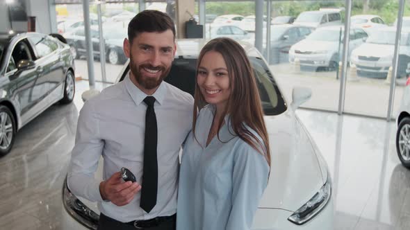 Visiting Car Dealership. Beautiful Couple Is Holding a Key of Their New Car, Looking at Camera and