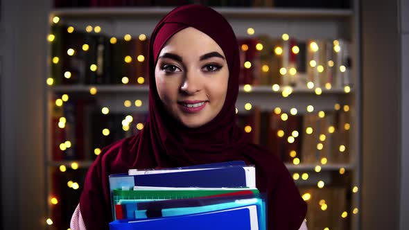 Close Up of Female Office Worker Standing on a Bookshelf with Garland Background and Holding Folders