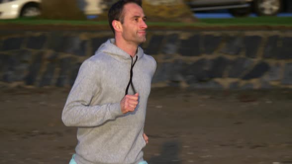 Slow motion tracking shot of young caucasian man running on the beach in Auckland, New Zealand