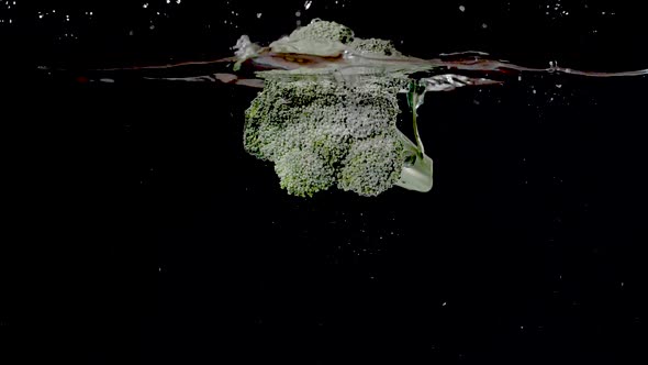 Colorful branch of broccoli being dropped into water in slow motion.