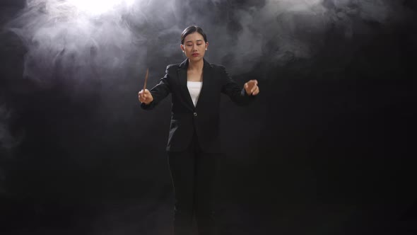 Asian Conductor Woman Holding A Baton Closing Her Eyes And Showing Gesture In The Black Studio