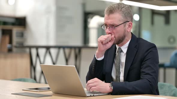 Sick Young Businessman with Laptop Coughing in Office