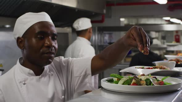 African american male chef garnishing dish and similing in restaurant kitchen