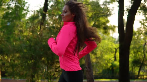 Young Woman in Bright Pink Jacket Running in the Sunny City Park Exercising Outdoors