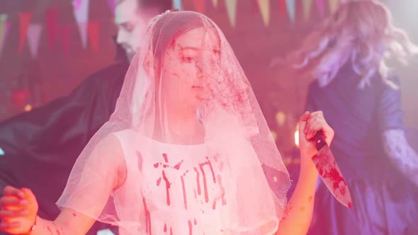 Young Girl in a Bloody Stained Bride Dress with a Veil on Her Face and a Bloody Knife As a Halloween