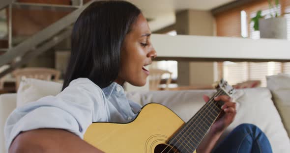 Mixed race woman on couch at home playing guitar and singing