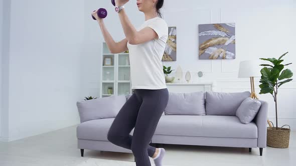 Woman with Funny Hairstyle in Sportswear which Doing Squat Exercises with Dumbells at Home