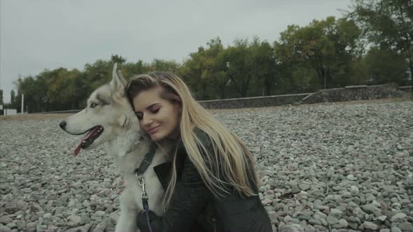 Young Cute Woman with Siberian Husky Dog Sitting on the Seaboard