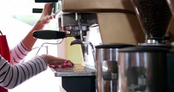 Waitress wiping espresso machine with napkin in cafe