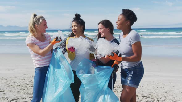 Diverse group of female friends putting rubbish in refuse sacks at the beach