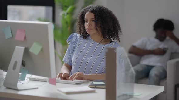 Focused African American Woman Typing Fast on Computer Keyboard with Blurred Man Surfing Internet on