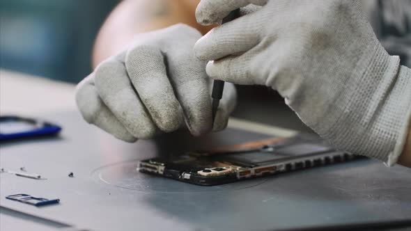 Repairman in White Gloves Disassembles Smartphone with Screwdriver in Workshop