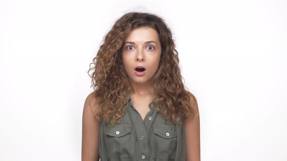 Lady in Grey Shirt with Curly Hair Expressing Worrying Looking Frightened Closing Mouth with Hand