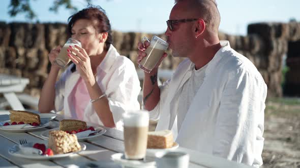 Adult Caucasian Man Drinking Tasty Cappuccino with Woman Sitting in Eco Park on Sunny Summer Day