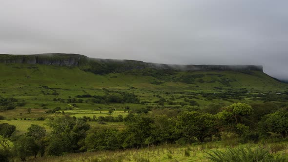 Time lapse of morning mist rolling over the green hills above and tree landscape in the foreground i