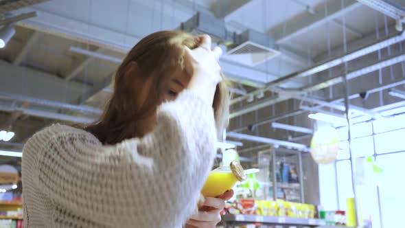 A Young Female Customer Reads the Composition of the Drink on the Juice Bottle