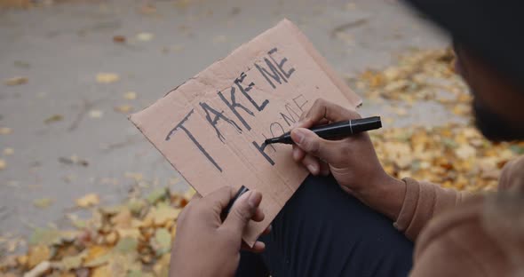 Young Black Hitchhiker Writing on Cardboard on the Road