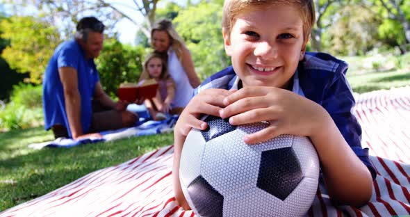 Smiling boy leaning on his football in picnic at park 4k