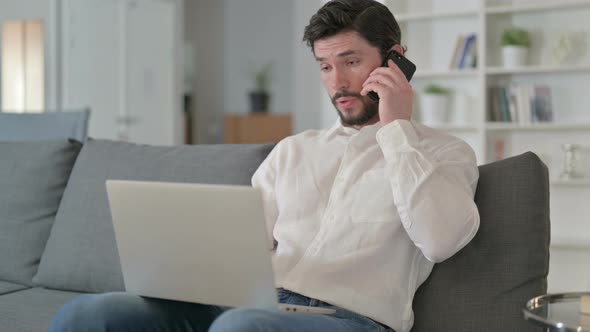 Man with Laptop Talking on Smartphone at Home