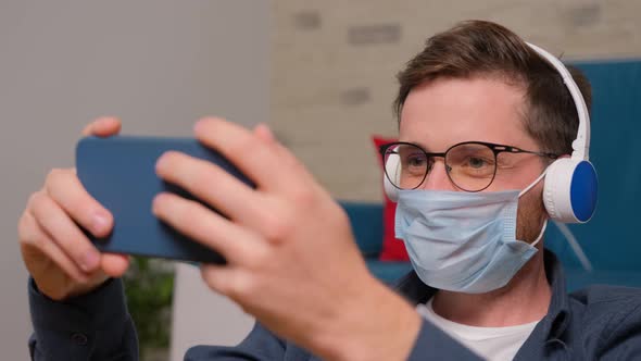 Young Man with a Medical Mask on His Face Talks Online with His Friends