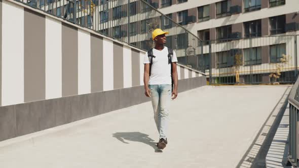 A Young AfricanAmerican Delivery Man Walks Down the City Street with a Yellow
