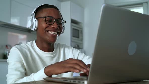 Happy Latin man having fun doing video call using laptop at home
