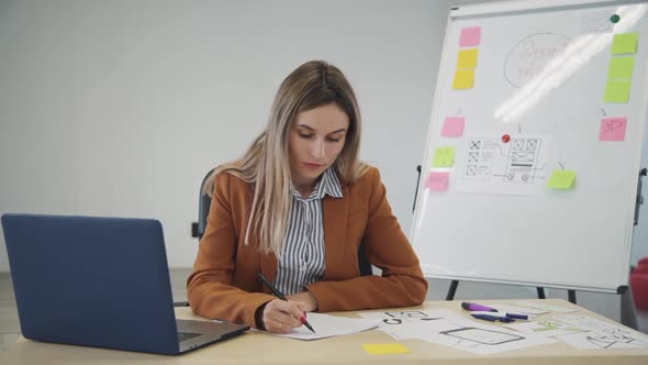 Young Caucasian Businesswoman Working with New Blueprint Sitting at Table in Office