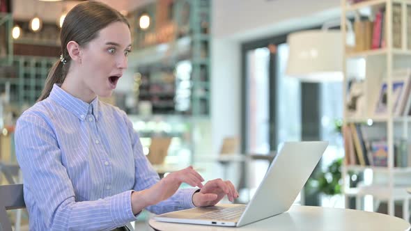 Young Businesswoman Celebrating on Laptop in Cafe