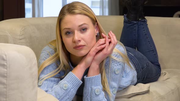 A Young Beautiful Woman Lies on a Couch and Looks at the Camera