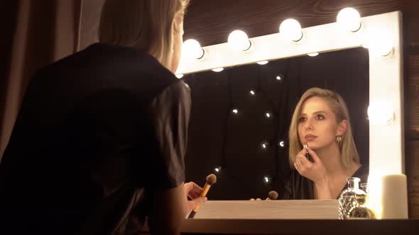 blonde  applying makeup with the mirror in dressing room