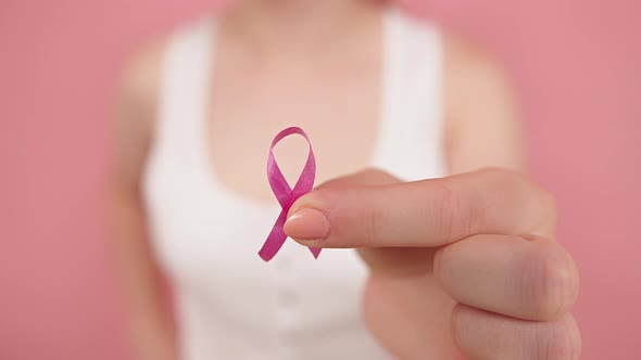 Young Woman Holding Symbolic Pink Ribbon Between Her Fingers. Breast Cancer Awareness Month, Pink