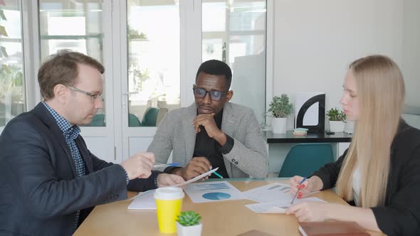Ethnic Diverse Business Team Discuss New Project Sitting By Table in Office