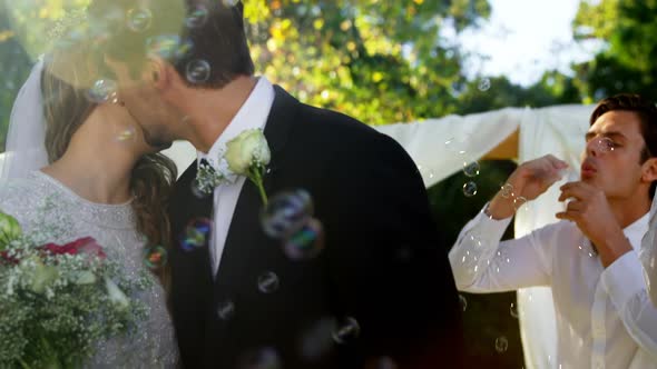 Bride and groom kissing while guest blowing bubbles