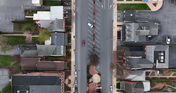 Aerial tracking of red car driving through American city, past USA flag in town square.