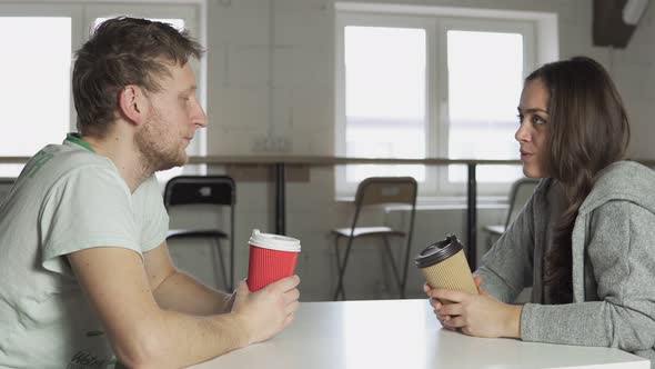 Two Friends are Sitting at the Table in Cafe Drinking Coffeetogo in Paper Cups and Talking