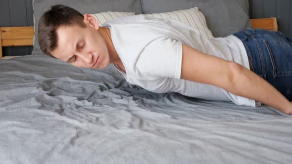 Tired Guy Falls Down on Bed with Grey Linen and Pillows