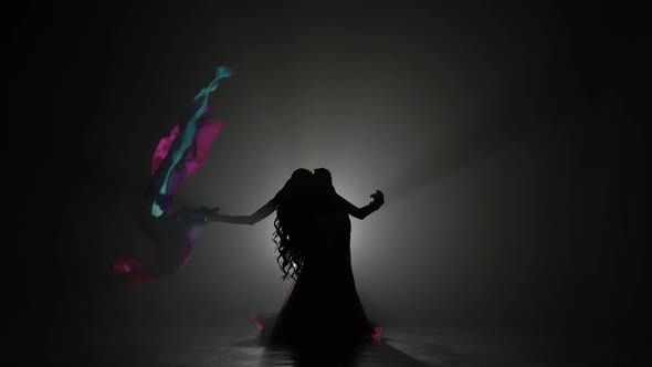 Girl with a Veil in Her Hands Dancing Belly Dance. Sihouette . Black Smoke Background