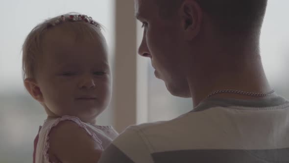 Back View of the Man Holding Little Baby Girl in His Arms in Front of Window Close-up. The Joys of