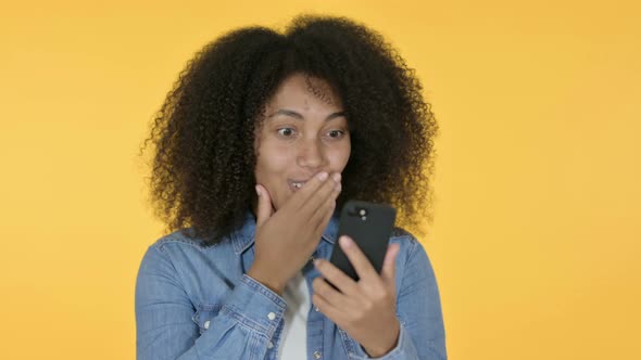 African Woman Celebrating on Smartphone, Yellow Background 