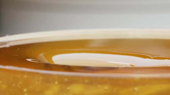 Close Up Fresh Thick Fluid Acacia Honey Pouring and Flowing From Wooden Dipper Spoon Over Black