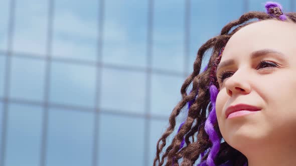Portrait of Woman with Dreadlocks Against Background of Glass Building