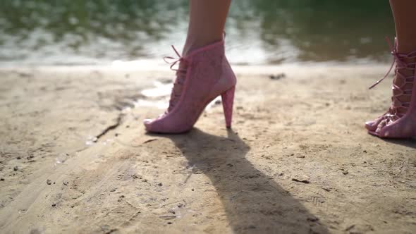 Woman Shod Pink Lace Shoes Is Walking Over Sand Coast of Lake or River at Sunny Day