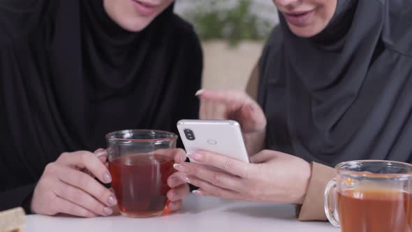 Close-up of Two Unrecognizable Muslim Women Using Smartphone, Talking and Smiling. Coexistence of