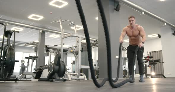 Athletic Guy Focused on Fitness Workout with Ropes in the Gym